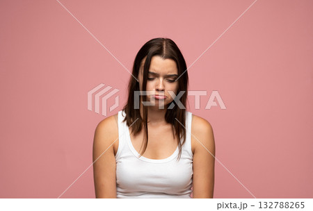 Sad emotion of young woman looking down with pouting lips on pink background Sad emotion of young woman looking down with pouting lips on pink background 132788265
