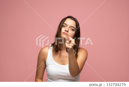 Confident emotion of young woman pointing finger forward in white tank top on pink background 132788270