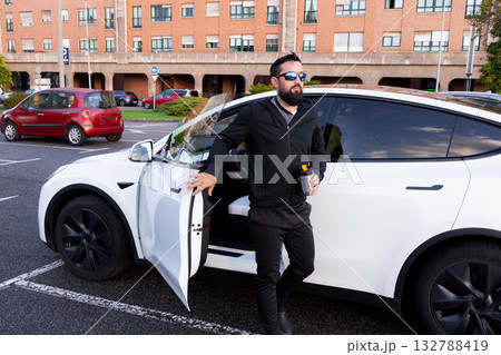 Young caucasian male exiting white electric car in urban parking lot 132788419