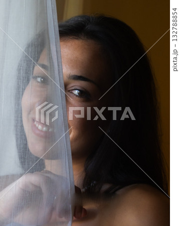 Young hispanic woman smiling peeking behind curtain 132788854