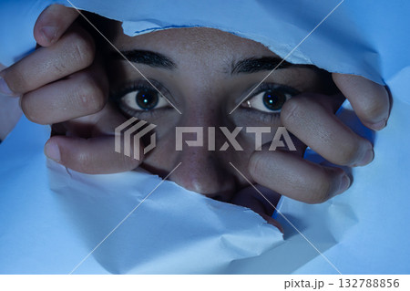 Woman peeking through torn paper with fearful eyes. Concepts of anxiety, hidden feelings Woman peeking through torn paper with fearful eyes. Concepts of anxiety, hidden feelings 132788856