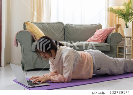 Healthy lifestyle woman teen maintains physical health, engaging in exercise workout at home, happily practicing yoga pose on mat, utilizing laptop for virtual sport training, promoting wellbeing. 132789174