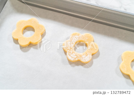 Cut-out flower cookies with holes in the center on parchment-lined baking sheet, pre-bake step for Easter Cookie Sandwich with Raspberry Buttercream. Cut-out flower cookies with holes in the center on parchment-lined baking sheet, pre-bake step for Easter Cookie Sandwich with Raspberry Buttercream. 132789472