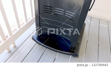 A vertical outdoor barbecue grill with a black and silver finish stands on a light-colored wooden deck. The bottom panel and curved design are clearly visible. A vertical outdoor barbecue grill with a black and silver finish stands on a light-colored wooden deck. The bottom panel and curved design are clearly visible. 132789482