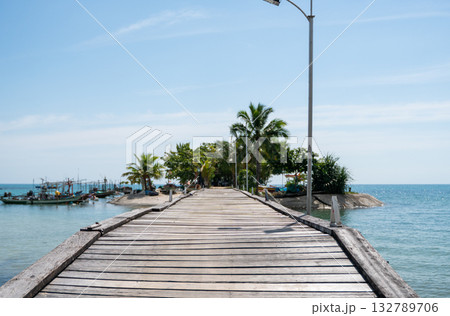 Wooden pier leading to small tropical island with palm trees and boats Wooden pier leading to small tropical island with palm trees and boats 132789706