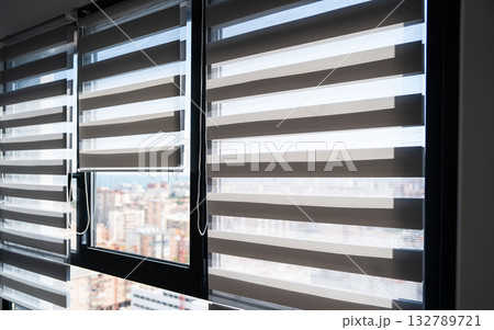 Zebra roller blinds partially open on modern apartment windows with cityscape view 132789721
