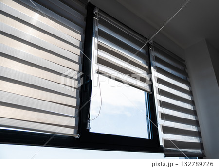 Large modern windows with zebra blinds partially open letting sunlight into bright interior Large modern windows with zebra blinds partially open letting sunlight into bright interior 132789726
