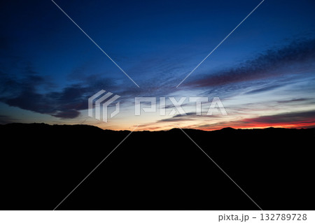 Dark blue sky after sunset with red horizon glow and soft moving clouds over distant hills Dark blue sky after sunset with red horizon glow and soft moving clouds over distant hills 132789728