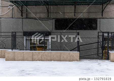 Snow falls heavily around the entrance of a basement store. The steps are slippery and the ground is blanketed in white indicating a winter storm's intensity. 132791819