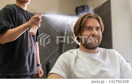 A barber sprays water on a male client's hair before a haircut. A barber sprays water on a male client's hair before a haircut. 132792109