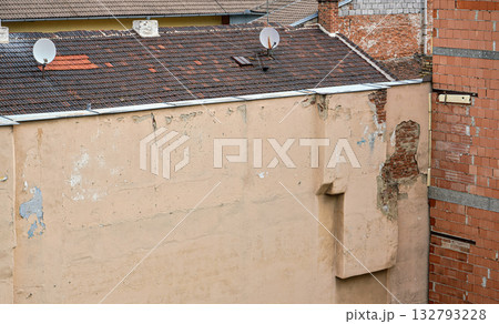 Old residential building wall, paint peeling, some bricks visible under plaster, tv satellite dishes on roof 132793228