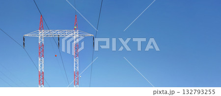 Red and white steel power pylon construction with high voltage cables against blue sky. Wide banner for electric energy industry with space for text on right side 132793255