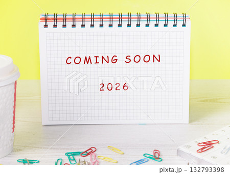 A notebook sits on a desk. It displays the words Coming Soon and the year 2026. There are paperclips scattered around it, and a beverage cup rests nearby A notebook sits on a desk. It displays the words Coming Soon and the year 2026. There are paperclips scattered around it, and a beverage cup rests nearby 132793398