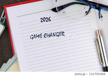 Open notebook displays the year 2026 and the phrase GAME CHANGER, accompanied by glasses and a pen, suggesting upcoming plans on a desk surface 132793408