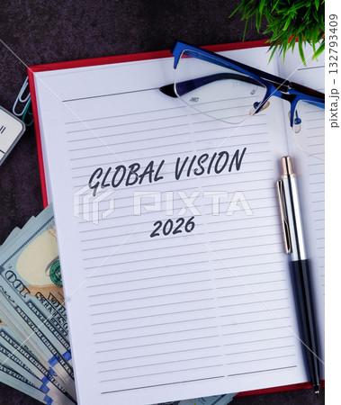 A notebook displays Global Vision and the year 2026. A pen and glasses are resting on top, with currency tucked inside. A small green plant sits near the top right corner A notebook displays Global Vision and the year 2026. A pen and glasses are resting on top, with currency tucked inside. A small green plant sits near the top right corner 132793409