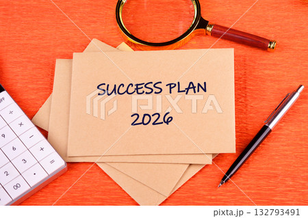 The 2026 Success Plan unfolds with a pen, a magnifying glass, and calculator nearby, hinting at calculations and reviews, all set against a textured orange backdrop 132793491