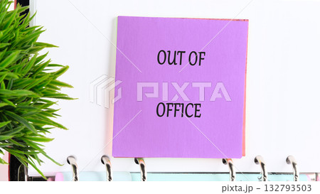 A lavender note boldly states OUT OF OFFICE, fastened to a ringed notebook next to a bright green plant, announcing a well deserved break from the daily grind 132793503
