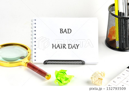 At the office a white notepad displays bad hair day. Nearby are a magnifying glass, crumpled papers, a pen holder with pens, and a calculator 132793509