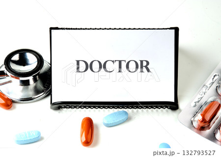 doctor is written on a sign. A stethoscope and pills are arranged on a white surface, suggesting healthcare, medical treatment, or pharmaceutical products for patient wellbeing doctor is written on a sign. A stethoscope and pills are arranged on a white surface, suggesting healthcare, medical treatment, or pharmaceutical products for patient wellbeing 132793527