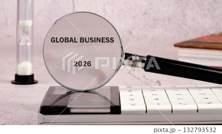 Magnifying glass over a calculator displays Global Business 2026 with an hourglass and books nearby, suggesting planning for the future in the Global market 132793532