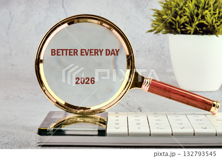 A magnifying glass resting on a calendar displays the words BETTER EVERY DAY and the year 2026. A potted plant sits in the background, adding to the hopeful scene A magnifying glass resting on a calendar displays the words BETTER EVERY DAY and the year 2026. A potted plant sits in the background, adding to the hopeful scene 132793545
