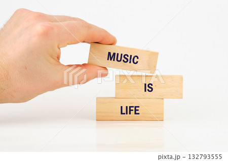 A hand carefully places a wooden block labeled MUSIC atop two other blocks that read IS and LIFE, conveying the message that music is essential A hand carefully places a wooden block labeled MUSIC atop two other blocks that read IS and LIFE, conveying the message that music is essential 132793555