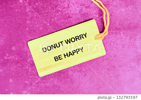 A light yellow tag displays DONUT WORRY BE HAPPY in black text. The tag is tied with a yellow string and rests on a textured magenta surface A light yellow tag displays DONUT WORRY BE HAPPY in black text. The tag is tied with a yellow string and rests on a textured magenta surface 132793597