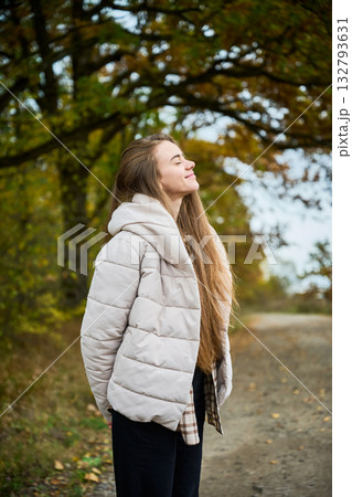 A young woman enjoys a peaceful moment outdoors, embracing the autumn air with a serene smile while surrounded by vibrant foliage. A young woman enjoys a peaceful moment outdoors, embracing the autumn air with a serene smile while surrounded by vibrant foliage. 132793631