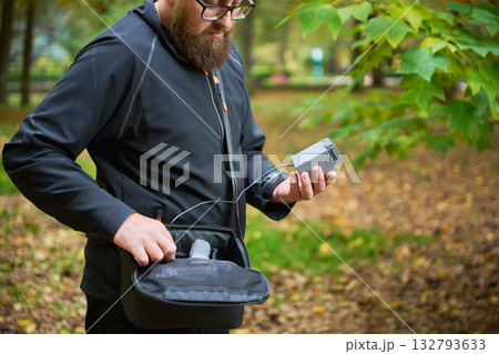 A man in a black jacket inspects his gear in a spacious park filled with colorful autumn foliage. He seems focused and ready for an outdoor adventure. A man in a black jacket inspects his gear in a spacious park filled with colorful autumn foliage. He seems focused and ready for an outdoor adventure. 132793633