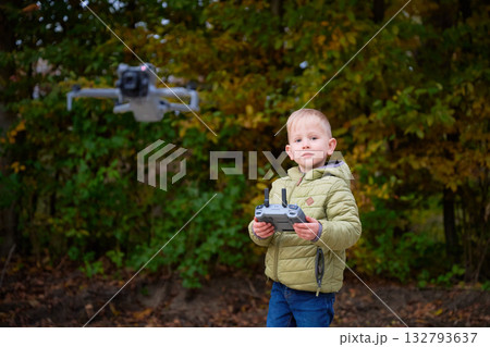 A young boy operates a drone with enthusiasm in a vibrant park filled with colorful autumn leaves. The sun shines brightly, enhancing the cheerful atmosphere. A young boy operates a drone with enthusiasm in a vibrant park filled with colorful autumn leaves. The sun shines brightly, enhancing the cheerful atmosphere. 132793637