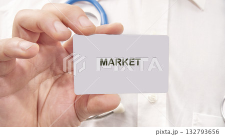 Doctor holds a card with the word MARKET in his hand. The scene is a clinical surrounding, possibly during health market research 132793656