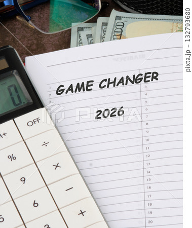 On a desk, money and a calculator accompany a note reading GAME CHANGER 2026, suggesting financial planning and future goals are being considered for the coming years 132793680