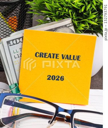 A bright yellow note saying CREATE VALUE 2026 rests beside cash, glasses, and a small plant, symbolizing the importance of innovation and financial growth in future endeavors 132793791