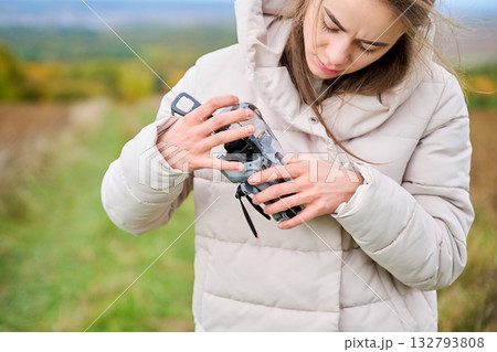 A young woman inspects her camera carefully as she enjoys a walk through a picturesque field filled with autumn colors. It is a calm afternoon. A young woman inspects her camera carefully as she enjoys a walk through a picturesque field filled with autumn colors. It is a calm afternoon. 132793808