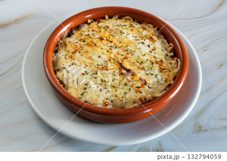 Creamy Kapsalon baked macaroni and cheese resting in ceramic ramekin with golden crust, sprinkled parsley, set on white plate over marble counter, warm homestyle comfort meal 132794059