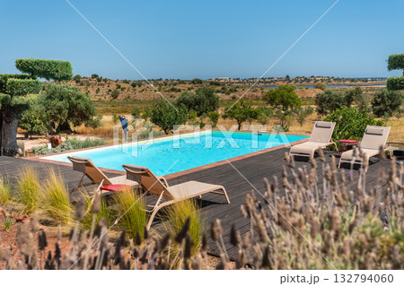 Peaceful infinity pool overlooking rural scenery, Tranquil blue water by lavender and olive groves, Serene infinity pool bathed in sunlight with rolling hills in distance 132794060