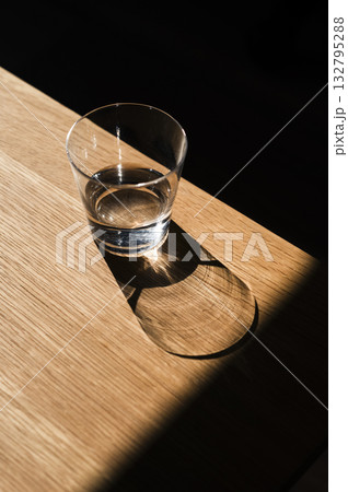 Glass of water casting shadow on wooden table 132795288
