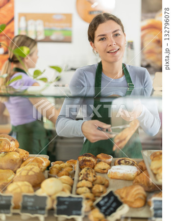 Young woman putting pastries in display case in cafe Young woman putting pastries in display case in cafe 132796078