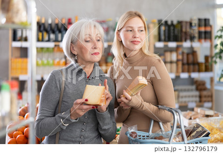 Adult daughter helps elderly mother choose delicious cheese in grocery supermarket Adult daughter helps elderly mother choose delicious cheese in grocery supermarket 132796179