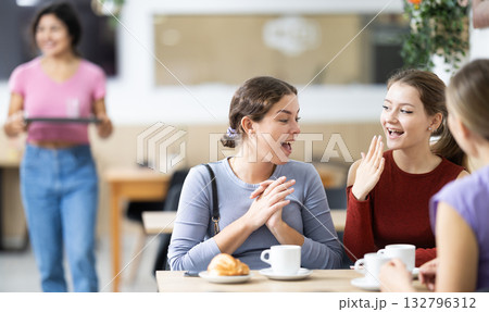 Three friends are chatting at table in cafe. They are drinking coffee or tea 132796312