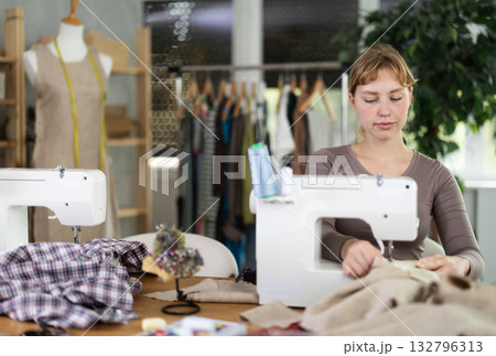 Young female dressmaker working with sewing-machine in tailor's workshop 132796313