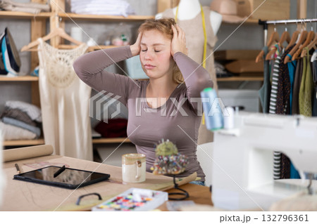 Tired female fashion designer sitting at table in sewing studio Tired female fashion designer sitting at table in sewing studio 132796361