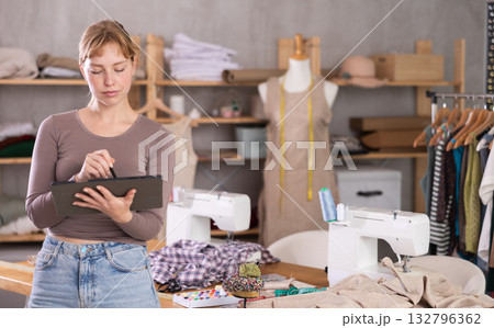 Female seamstress designing custom dress using tablet in studio Female seamstress designing custom dress using tablet in studio 132796362