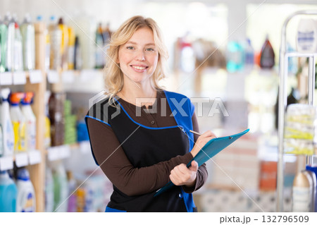 Beautiful diligent young girl saleswoman standing between shelves and doing inventory in hypermarket 132796509