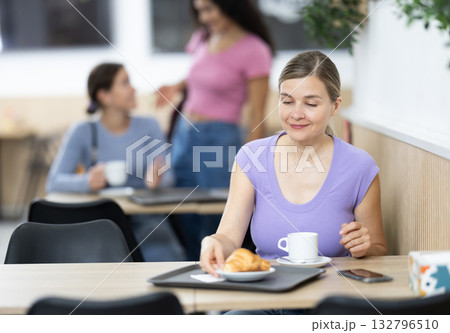 Young woman enjoying coffee and croissant in cafeteria 132796510