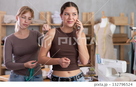 Female client chatting on phone while dressmaker taking body measurements Female client chatting on phone while dressmaker taking body measurements 132796524