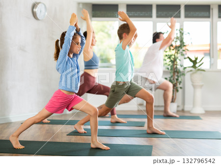 Mom, dad, daughter and son are standing in the warrior pose, Virabhadrasana 132796542