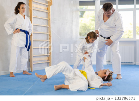 Preteen girl in kimono practicing throws in sparring with brother at family training 132796573
