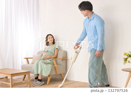 妊婦の女性と話しながら楽しそうに掃除機をかける若い男性 132797526