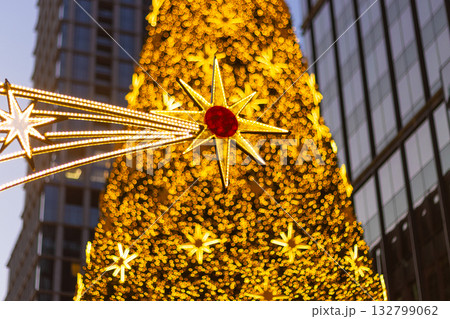 Christmas tree golden star decoration holiday. A close-up view of a festive outdoor tree covered in warm, yellow bokeh lights and a large, prominent, stylized star ornament 132799062